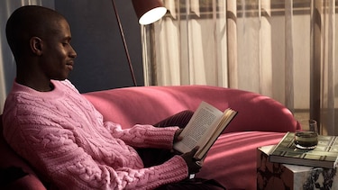 Man in pink sweater on pink couch, reading a book