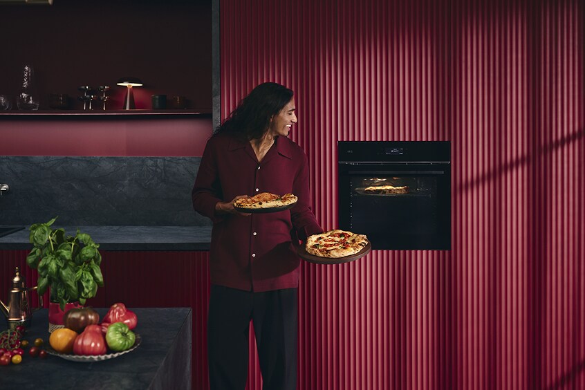 Egy nő, aki egy pizzát tart a sütő közelében
