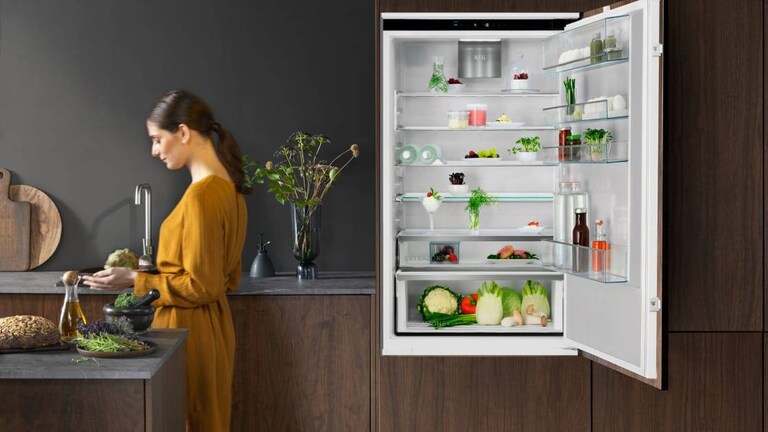 Nő áll a konyhában, a nyitott hűtő mellett